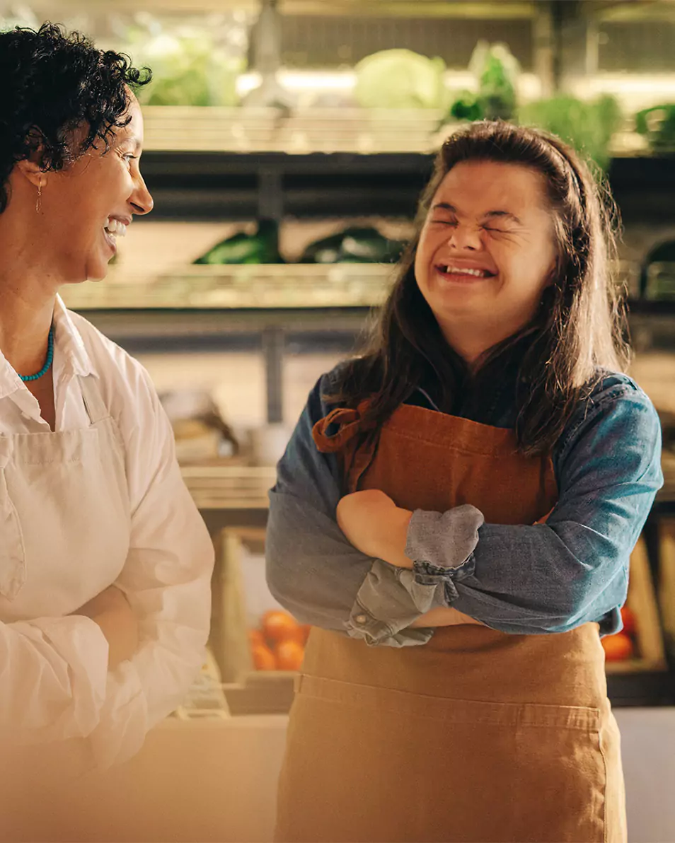 A down syndrome woman and her carer working in a fruit and veg shop, they are sharing a laugh
