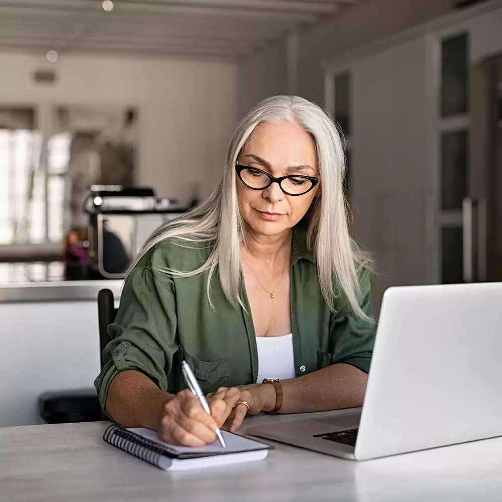 A woman taking notes while on her laptop at home