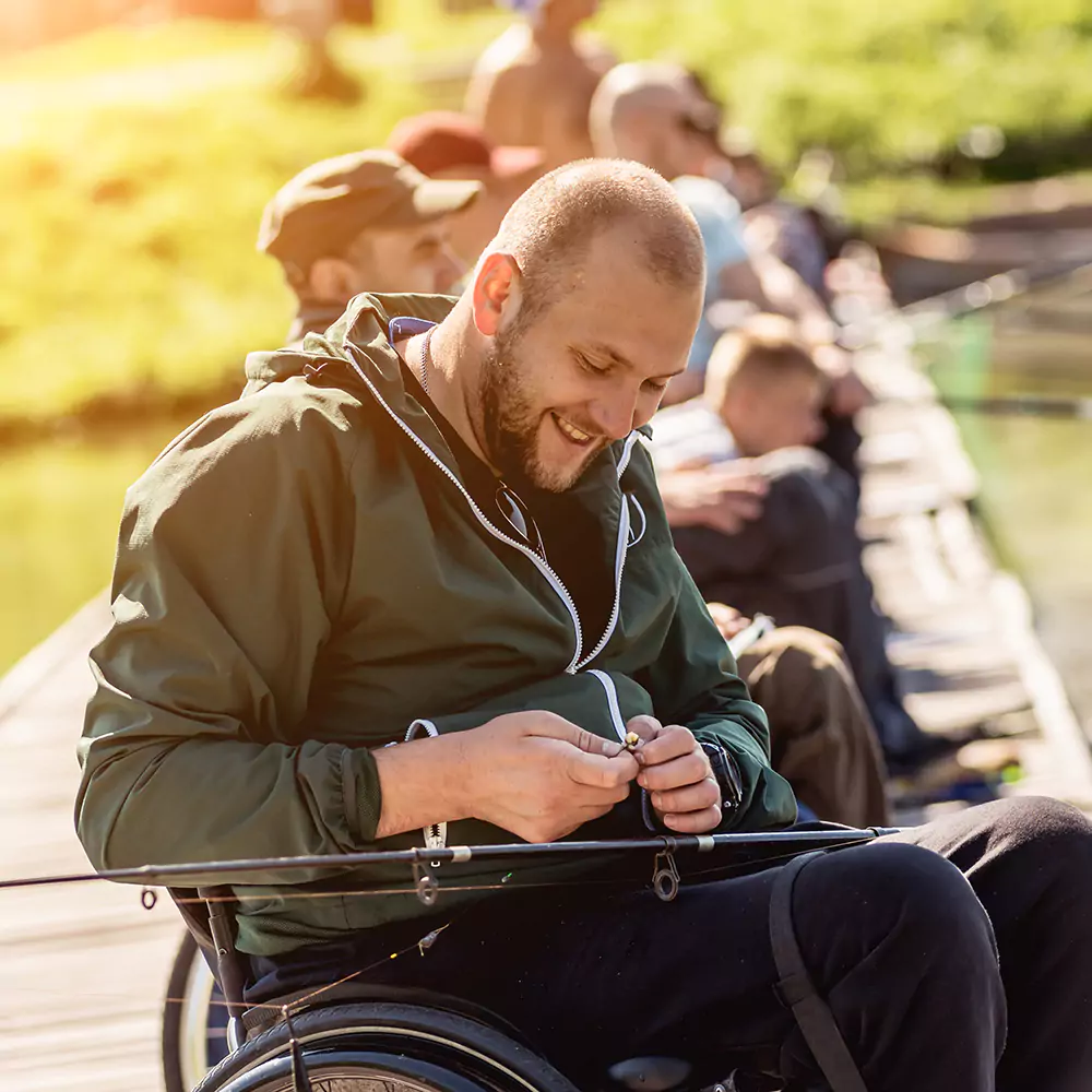 A disabled man in a wheelchair outdoors fishing with friends