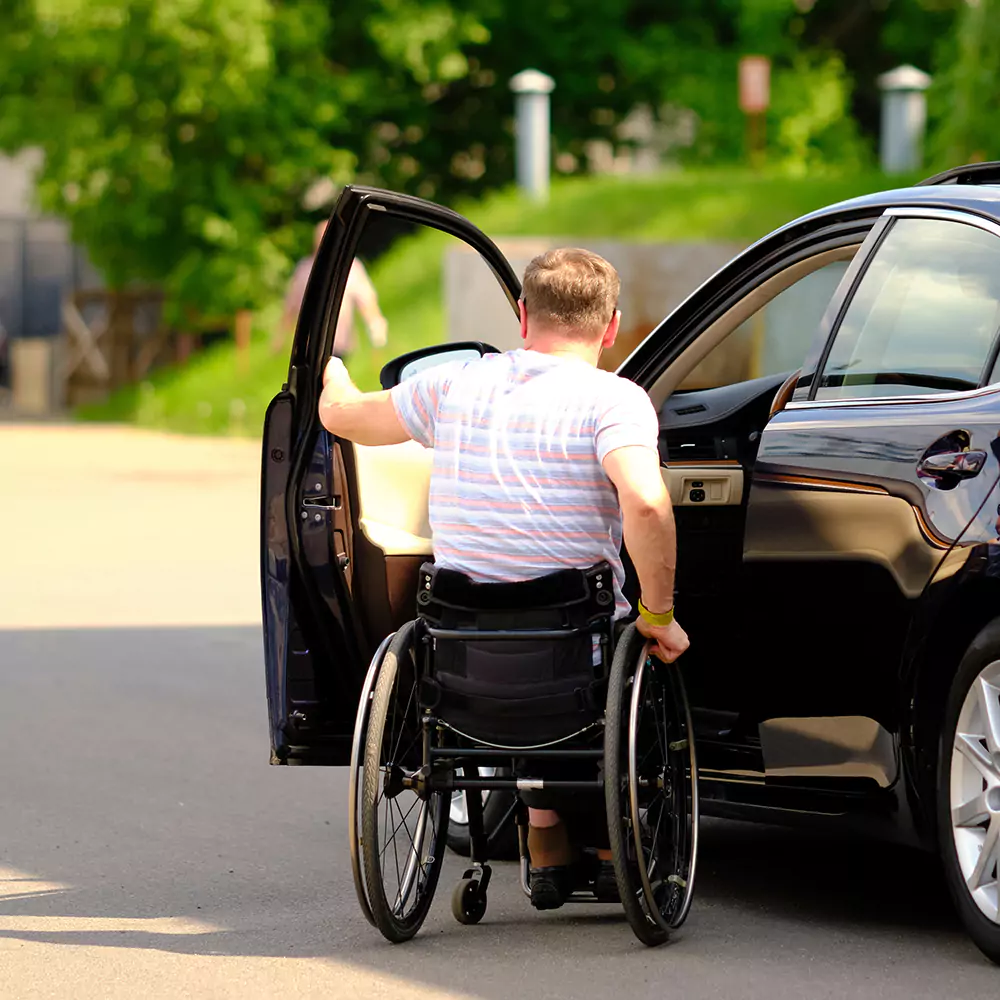 A disabled man leaving his wheelchair to enter into a car