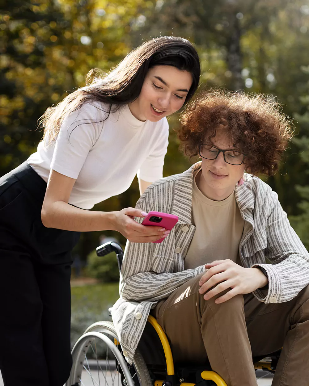 A disabled teenage boy in a wheelchair and his carer outdoors