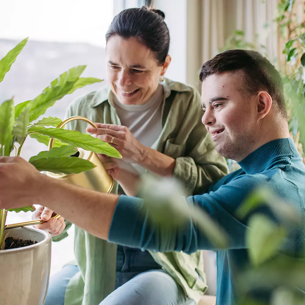 A down syndrome man with his female carer watering plants